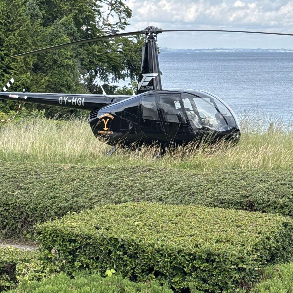 En helikopter p&aring; en gr&aelig;spl&aelig;ne med vand i baggrunden.