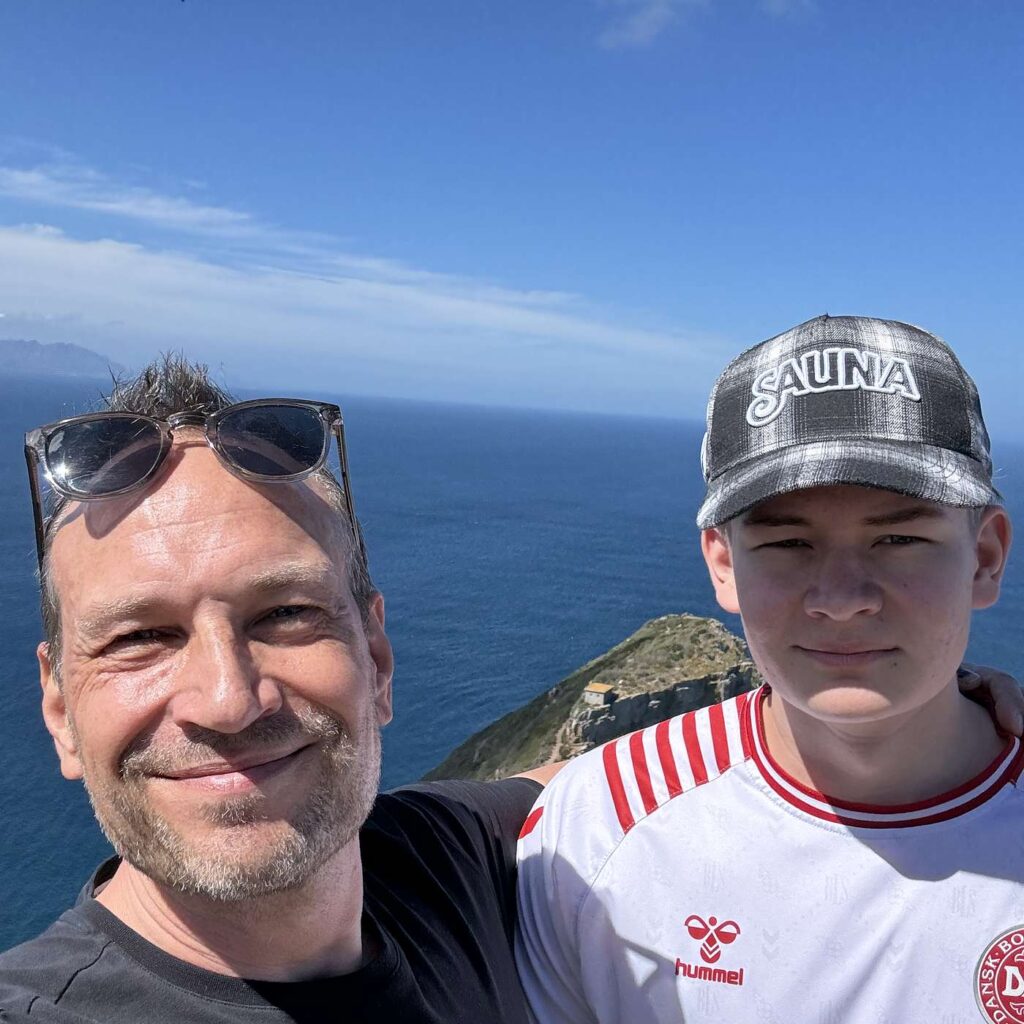 Martin Thorborg sammen med en ung mand med kasket og havet i baggrunden.