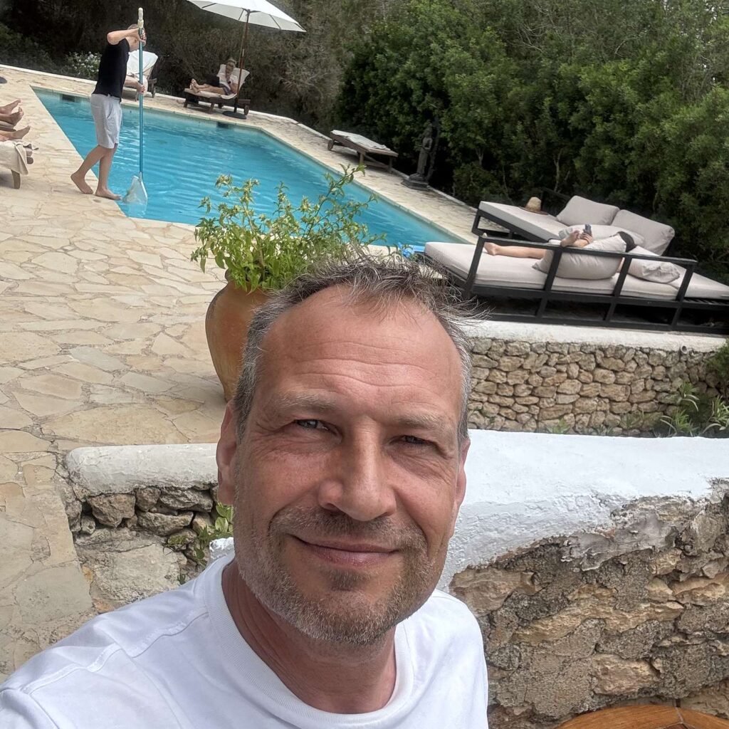 En mand renser en swimmingpool med et net, mens andre slapper af p&aring; liggestole.
