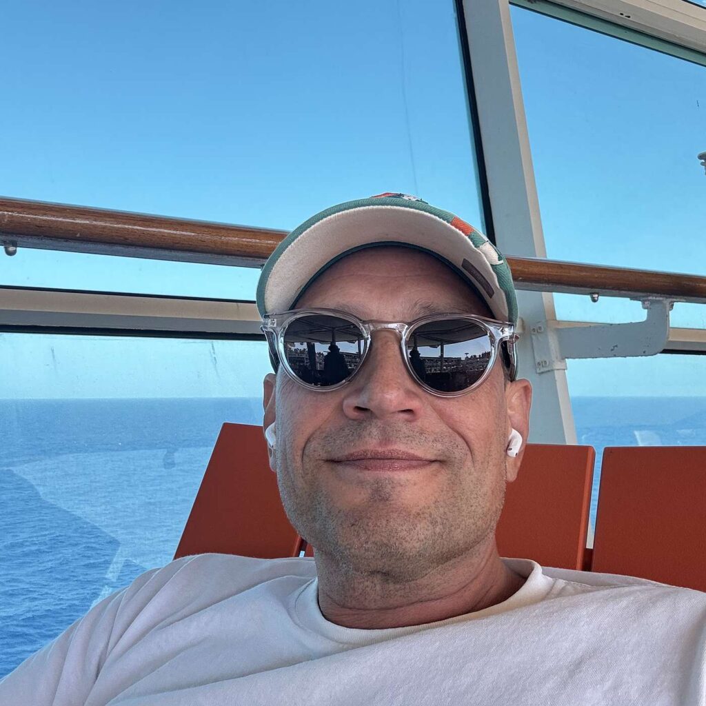 Martin Thorborg med kasket og solbriller med havet bag sig.