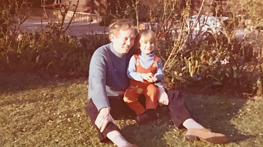Et gammelt familiefoto af en voksen og et barn i en have.
